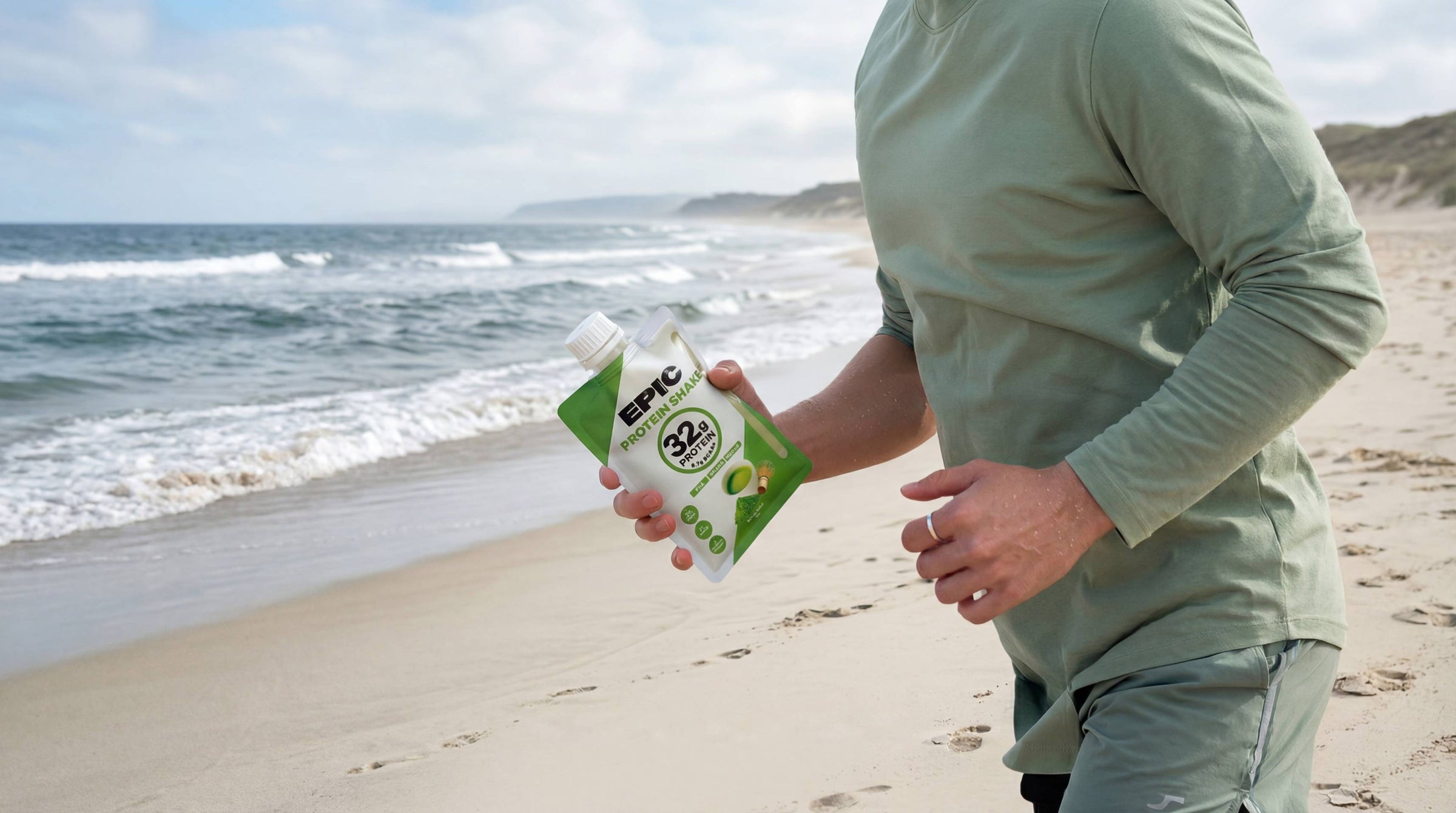 Person holding a BPA-free protein drink pouch on a beach after running to recover
